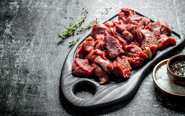 Sliced raw beef on a cutting Board with thyme and seasonings in bowls.