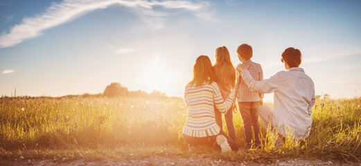 Family standing on the sunset on the field in natural park. - obrazy, fototapety, plakaty