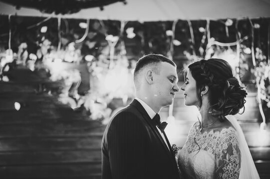 Wedding Vows. The bride and groom kissing on wooden wall background. Newlyweds standing in night ceremony under arch. Black and white photo.