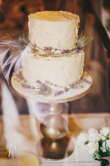 Stylish rustic wedding cake with lavender and thistle decor on vintage stand on table at wedding reception in restaurant. Modern beautiful provence wedding cake. Luxury catering at banquets