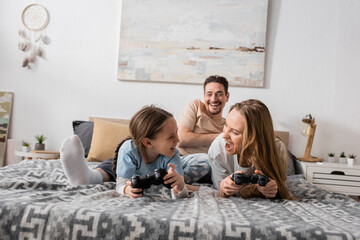 KYIV, UKRAINE - NOVEMBER 28, 2022: cheerful mother, father and excited child playing video game in bedroom
