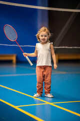 Little girl three years old playing badminton in sport wear on indoor court 