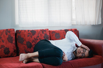 Asian young upset depressed man sitting alone in living room at home. Attractive unhappy male feeling very sad, lonely and frustrated with life problem think of money debt, bankruptcy.
