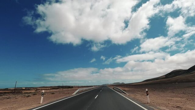 Cinematic driving concept on empty road in the desert with blue sky and white clouds in background. Concept of travel and adventure in car perspective. Freedom and scenic destination landscape