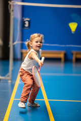 Little girl three years old playing badminton in sport wear on indoor court  - obrazy, fototapety, plakaty