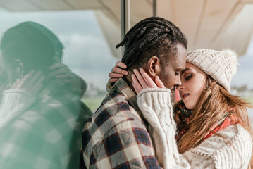 Close up portrait of a young interracial couple trying to kiss where woman is holding her boyfriend face in her hands close outside while dating
