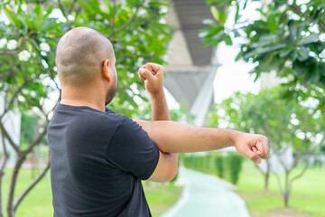 Back side young asian male relaxing in sports outfits black stretching before workout in the park get a healthy lifestyle. Healthy sporty man warming and stretching arms and looking away.