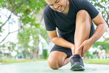 Young male in sports outfits black injured his ankle during exercise in the park. Low section of...
