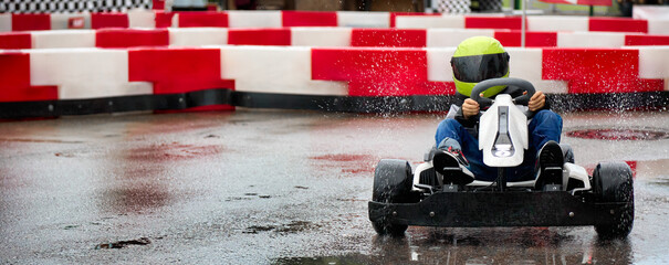 Brave young racer at high speed passes the turn of the karting track on a racing car. Young karting racer on the circuit in a protective helmet - obrazy, fototapety, plakaty