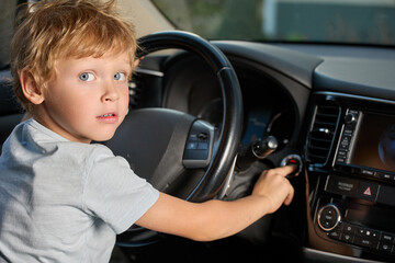 Blue-eyed boy sits in the driver's seat inside the car, presses his finger on the ignition button....