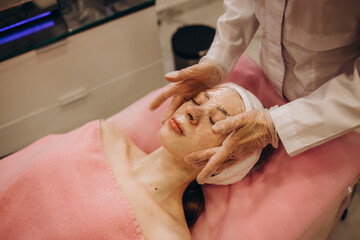 Cosmetologist applying mask on woman's face in beauty salon