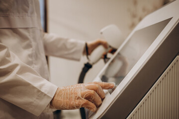 Obraz premium Cosmetologist's hand adjusting a modern laser apparatus in a beauty salon. Procedure of skin cleansing by laser pulses. The process of photothermolysis, warming the skin. Hardware