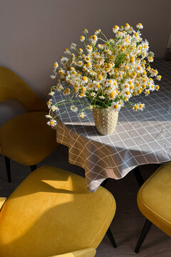 A bouquet of delicate chamomile in a ceramic vase. Morning light in the room. A vase with white flowers on a beige wall on the table. Interior. A greeting card. Copy space. Vertical photo