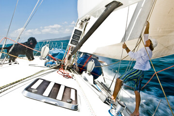A sailor adjusts a sail with a dog on the bow during a race