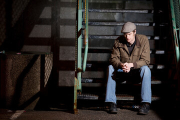 Salmon Arm, BC - A young man in coat and cap sits on metal stairs beside a garbage can at a local high school.