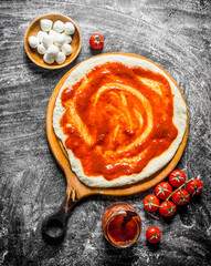 Raw pizza. Rolled out dough with tomato paste, mozzarella and fresh tomatoes.