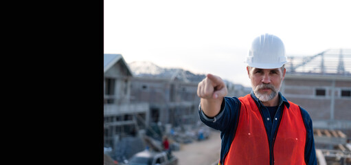Banner of senior engineer wearing white helmet, pointing his finger in the air with home construction background at real estate project. Professional elderly civil engineering checking project plan.