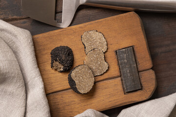Whole and sliced black truffles mushroom on wooden board on dark brown table, flat lay, copy space.