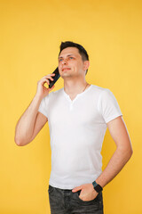 handsome young man holding a phone in his hand, talking emotionally on the phone on a yellow plain background.
