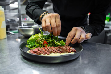 Obraz na płótnie Canvas chef hand cooking Roast beef salad with vegetables on restaurant kitchen
