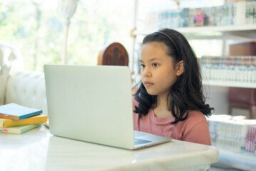 asian undergraduate teen girl student study in library with laptop books doing online research for coursework, online education e-learning concept. teenage female student preparing for exams at home.