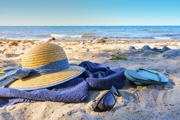 Straw hat and flip flops on a blue towel on the natural beach on the sea, tourist resort on the...