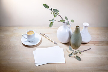 Three vases, sage leaf branch and coffee cup, mock- up of white greeting cards on a wooden table or...