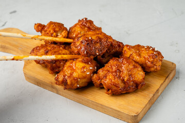 Fried chicken pieces in Asian sauce close-up and chopsticks that hold a piece of chicken. light table