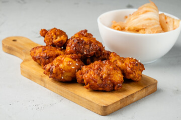 Pieces of chicken fillet in spicy sauce on a wooden board and a cup with kimchi.
