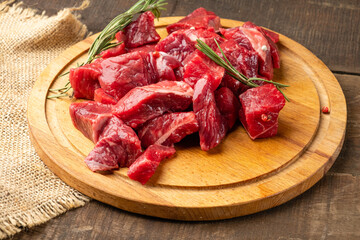 Fresh beef fillet cut into cubes for further cooking lie on a round wooden board.
