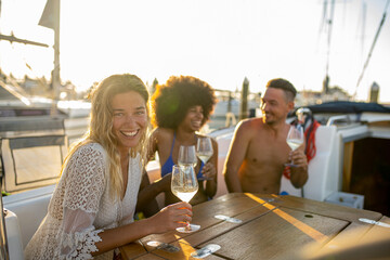 Party moments on a yacht, young blonde woman smiles and looking at the camera, sunlight through the sails of the boats in the harbor