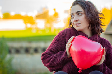 Mujer joven de raza caucásica con el pelo corto agarrando un globo rojo con forma de corazón que...