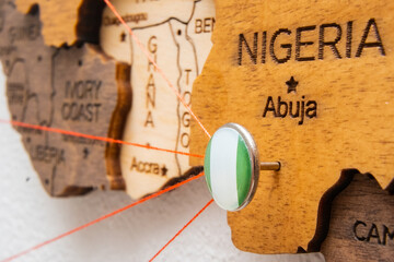 Nigeria flag on the pushpin with red thread showed the paths of movement or areas of influence in the global economy on the wooden map. Planning of traveling or logistic concept. Network connection. 