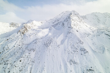 Snow covered peaks of mountains during winter on a sunny day with clouds in Fluela Pass, Davos, Switzerland.