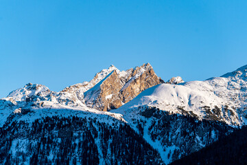 Sun hitting sharp mountain peaks covered in snow during winter on a sunny day near Guarda village, Switzerland.