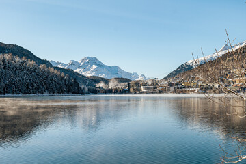 View of the town of St. Moritz and a lake, forest and mountains during winter with snow on a sunny...