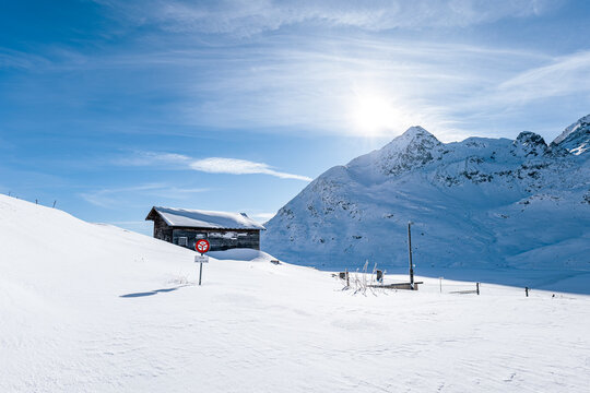 Wooden Cabin In The Mountains During Winter Covered In Fresh Snow On A Sunny Day In Switzerland.