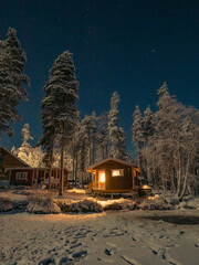 Red wooden cabin in winter forest during nighttime in Rovaniemi, Finland.