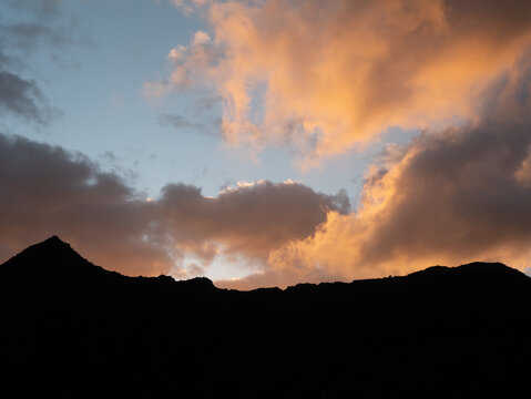 Sunset orange clouds rolling over mountain.