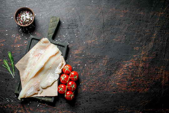 Fish fillets on the paper with a knife, rosemary and spices in a bowl.