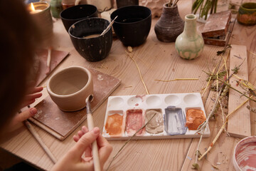 faceless woman paints a clay bowl or Plate.