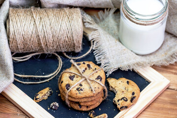 Top view of chocolate chip cookies with glass of milk on wooden background