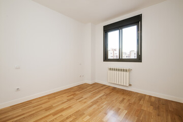 Fototapeta na wymiar Room of an empty house with glossy oak parquet floors with black anodized aluminum window and white aluminum radiator under the window