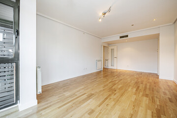 Room of an empty house with gloss oak parquet floors with black anodized aluminum window and aluminum radiator on the walls, white access door and carpentry of the same color