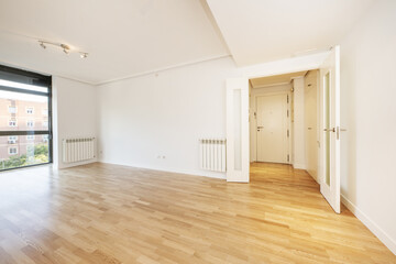 Room of an empty house with gloss oak parquet floors with black anodized aluminum window and aluminum radiator on the walls, white access door and carpentry of the same color