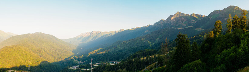 Fototapeta na wymiar Panorama: View of the Caucasus Mountains at the Rosa Khutor resort at sunset in summer