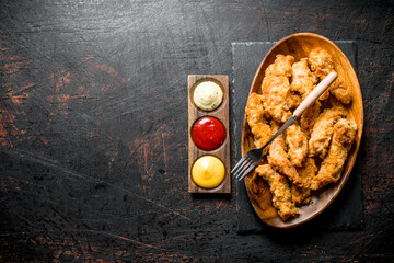 Chicken strips on a plate with a fork and different sauces.