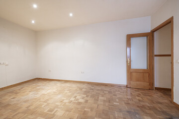 Living room of an empty house with oak parquet floors laid in a checkerboard pattern and matching oak doors