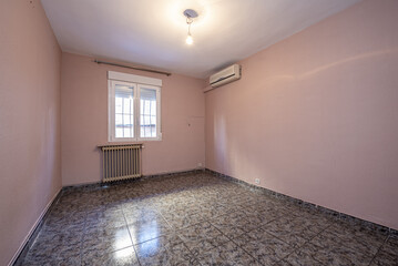 Long empty room with ugly dark tiled floor and pale pink painted walls, cast iron radiator under...
