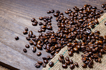 Roasted coffee beans and hemp fabric on brown wooden board.